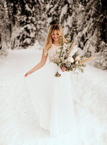 Braut im weißen Kleid in Schneelandschaft mit Brautstrauß