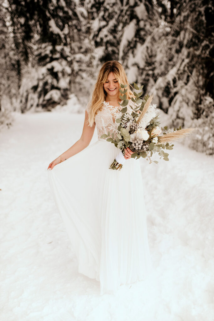 Braut im weißen Brautkleid im Schnee mit winterlichem Brautstrauß